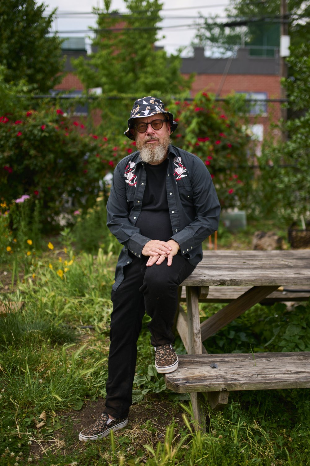 A gardener poses for a photo, sitting on the corner of a wooden table.