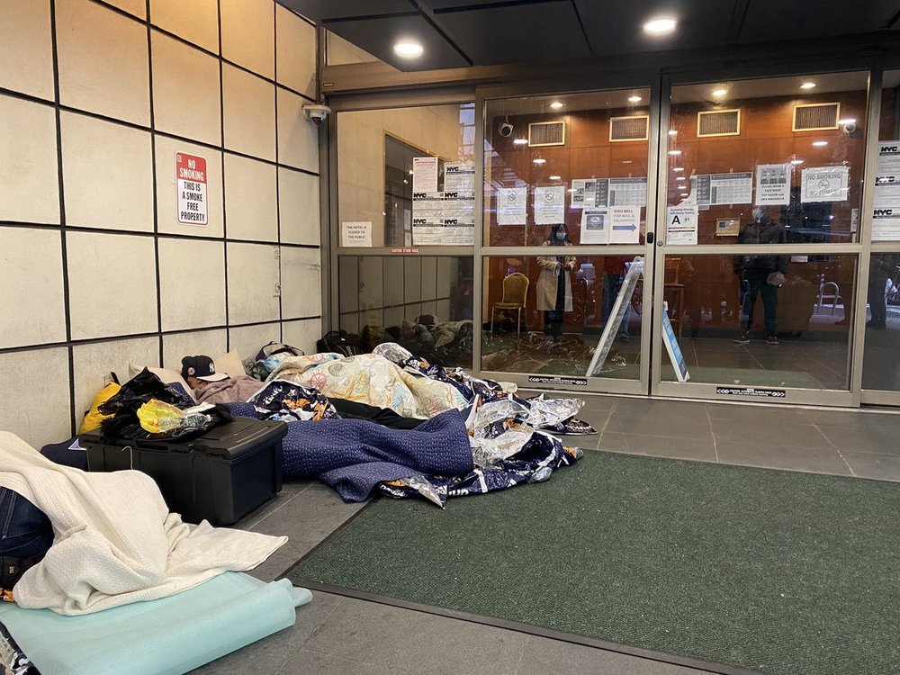 People sleep outside on the sidewalk in New York City.