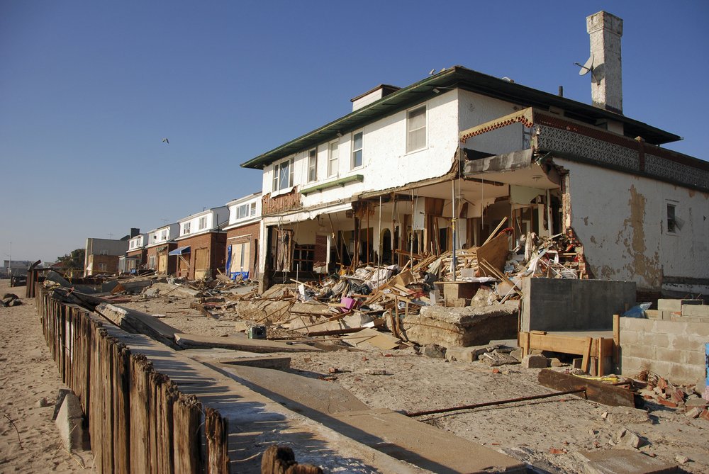 A beachfront mansion stands with its foundation exposed, and the lower half of the building hollowed out.