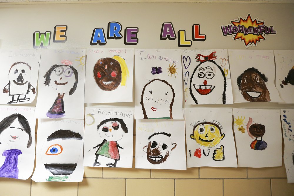 A school wall that features hand-drawn pictures, many of them self-portraits. The wall is titled in colorful letters: "We are all wonderful!"
