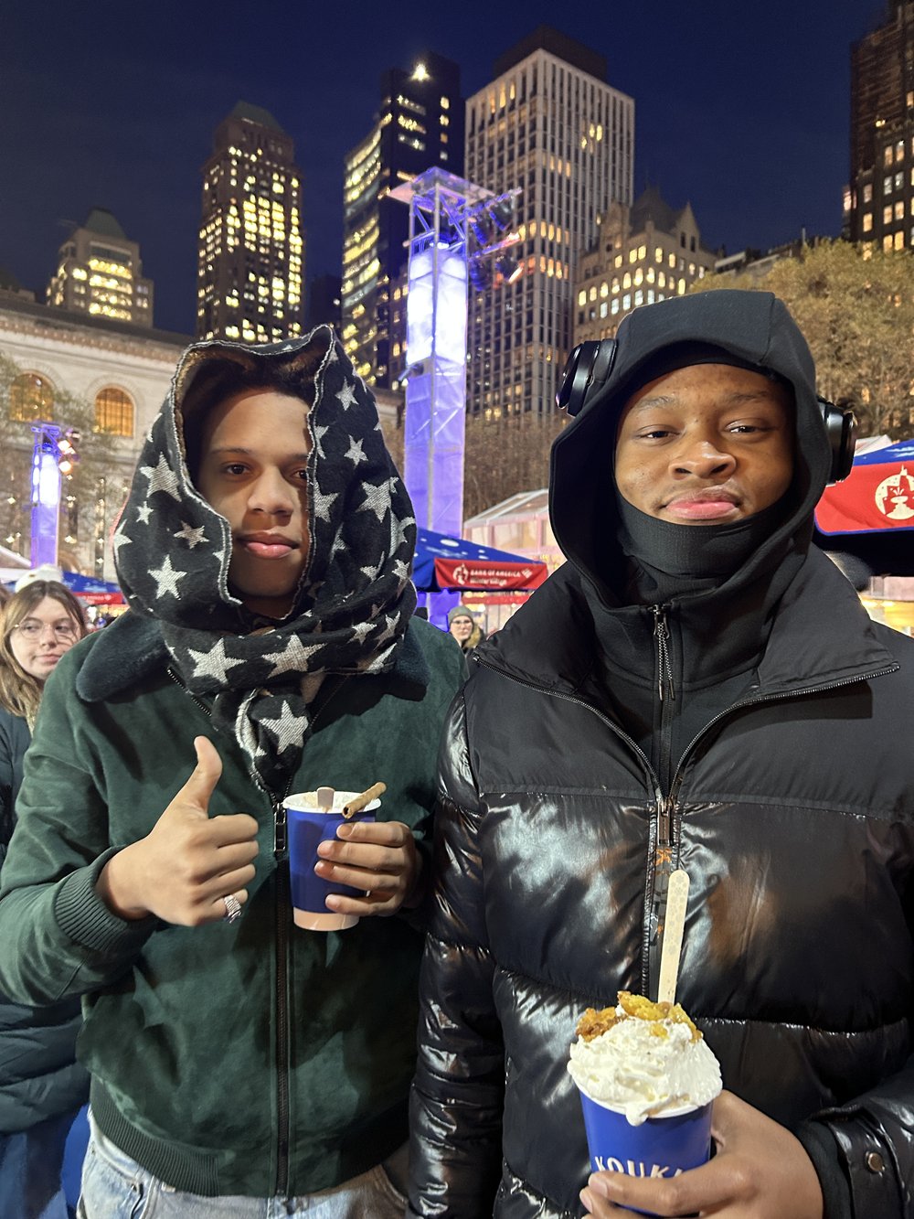 Two friends stand next to each other holding hot chocolate.