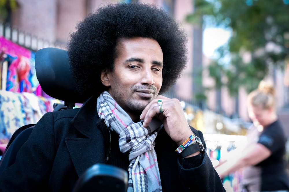 A man sitting down with a plaid scarf and black jacket.