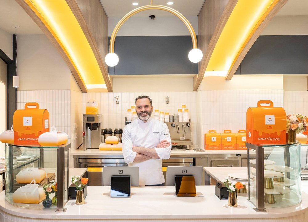 A man stands in a bakery surrounded by orange pastry boxes.