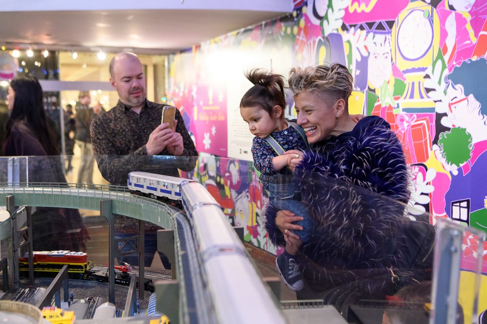 A woman and child look at a toy train while a man takes their picture.