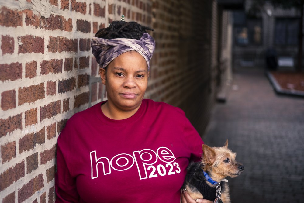A woman stands in the courtyard of her apartment building, holding her dog.