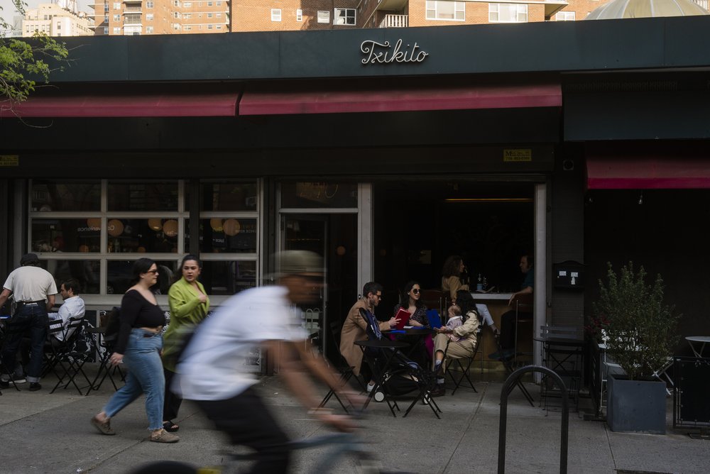 The exterior of a restaurant called Txikito. A bike rider rides past as diners sit outside.