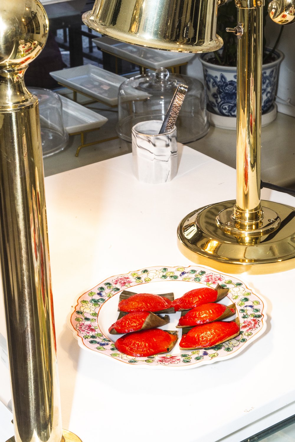 A plate of shiny (gelatinous) red dumpling-looking desserts sit on a plate on a counter. The scene is framed by the gold trim of a light fixture.