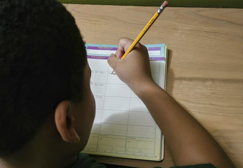 A young person hold a pencil in their right hand and writes in their planner.