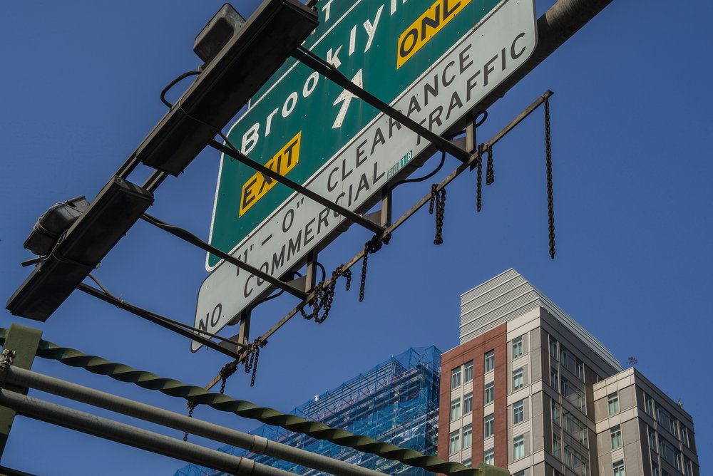An elevated road sign with seven chains wrapped around the bottom beam of the sign