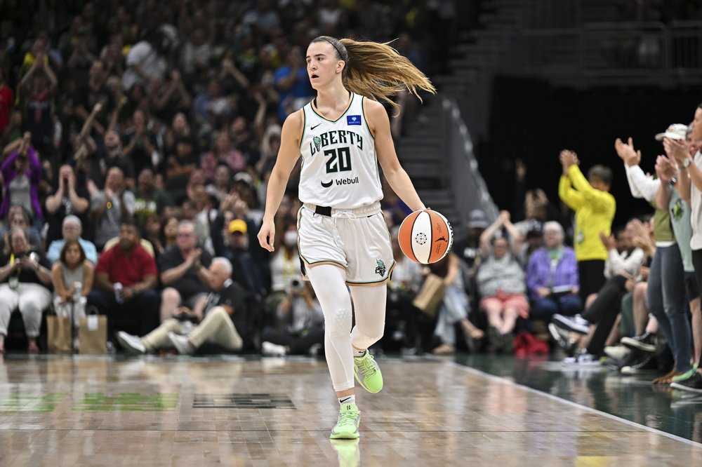 A woman in a white basketball uniform dribbles a basketball on the court.