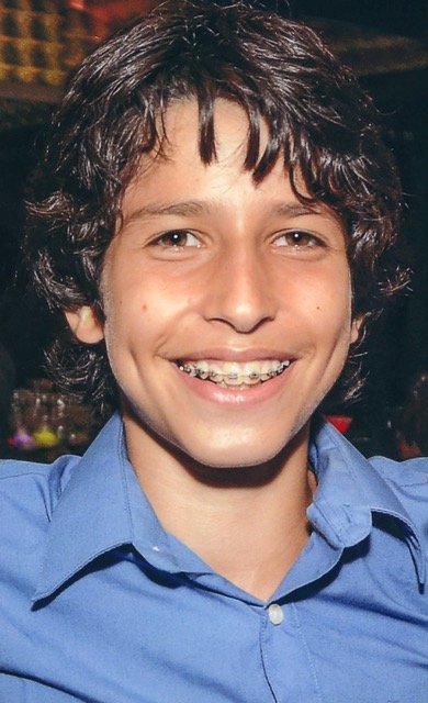 A close-up photo of 12-year-old Sammy Cohen Eckstein. Sammy is smiling. He has braces and bright brown eyes. Sammy is wearing a blue shirt.