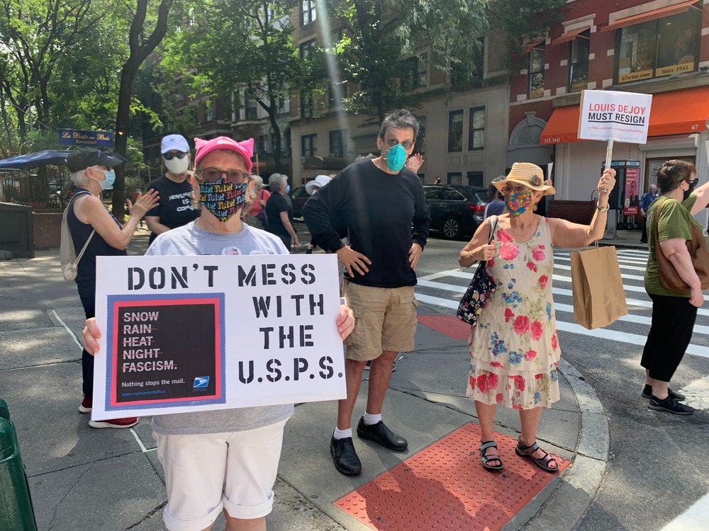 Protesters calling to ensure the U.S. Postal Service is meddled with hold up signs that read "Don't Mess With The U.S.P.S." and "DeJoy Must Resign."