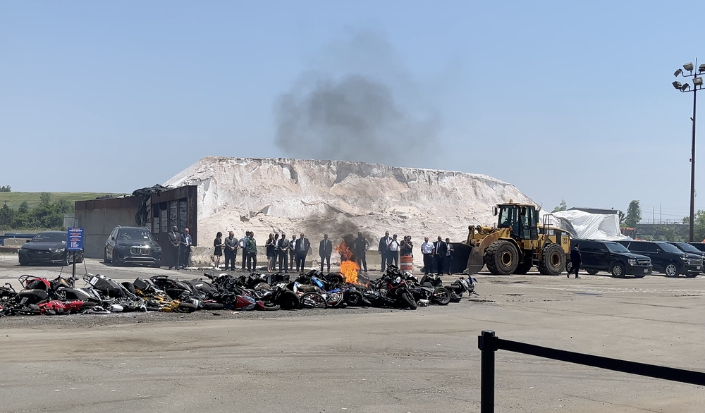 A pile of e-bikes on fire as officials look on.