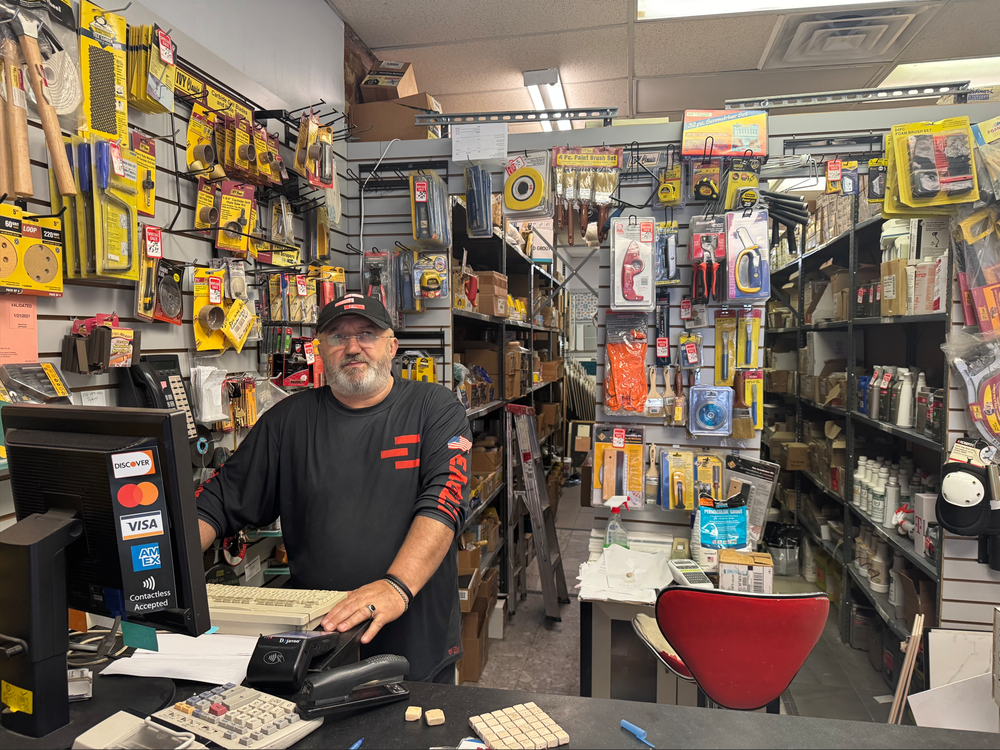 A man standing behind the couner in a tile store filled with tools.