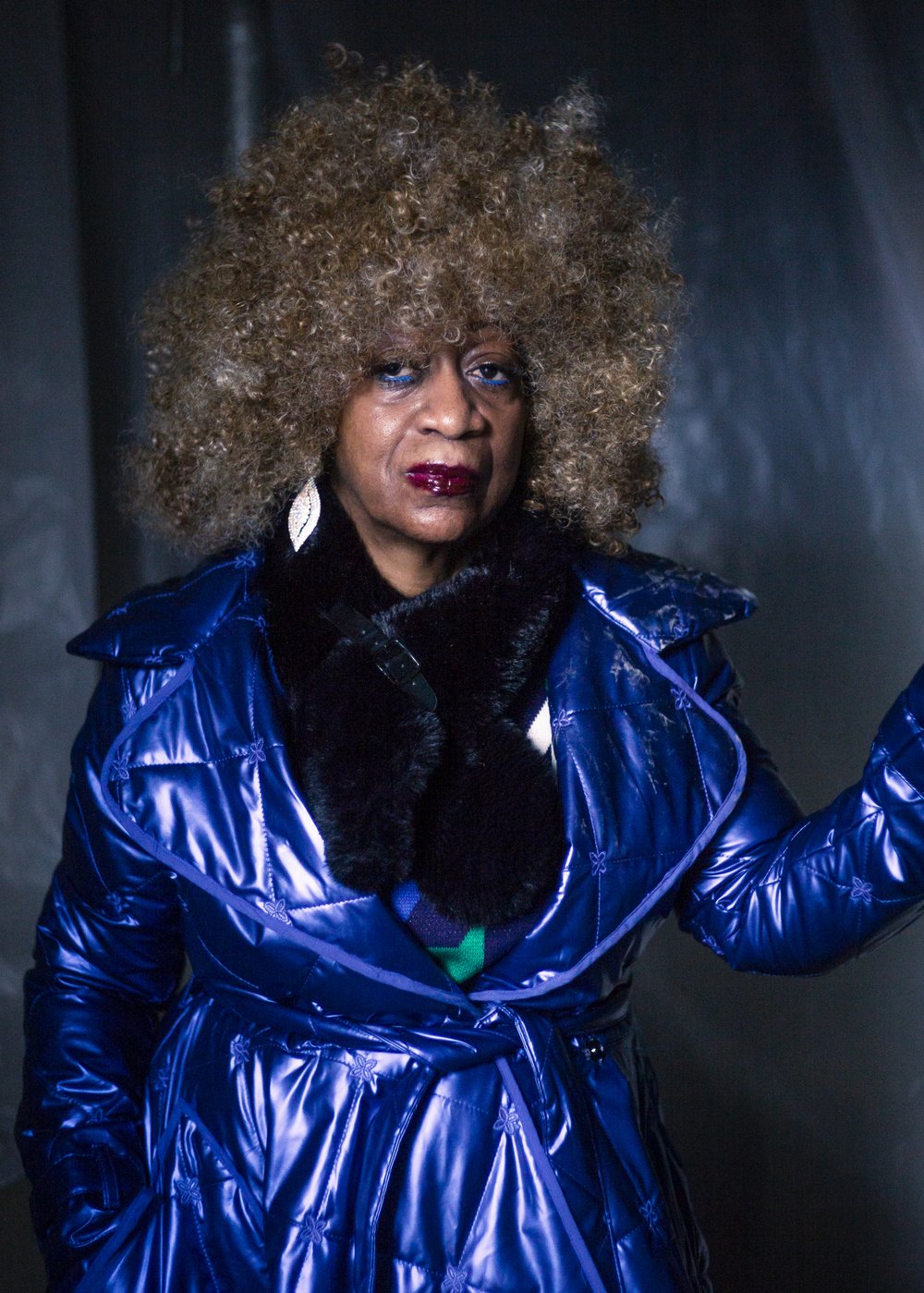 A woman with a large, curly blonde afro, and a reflective blue jacket.