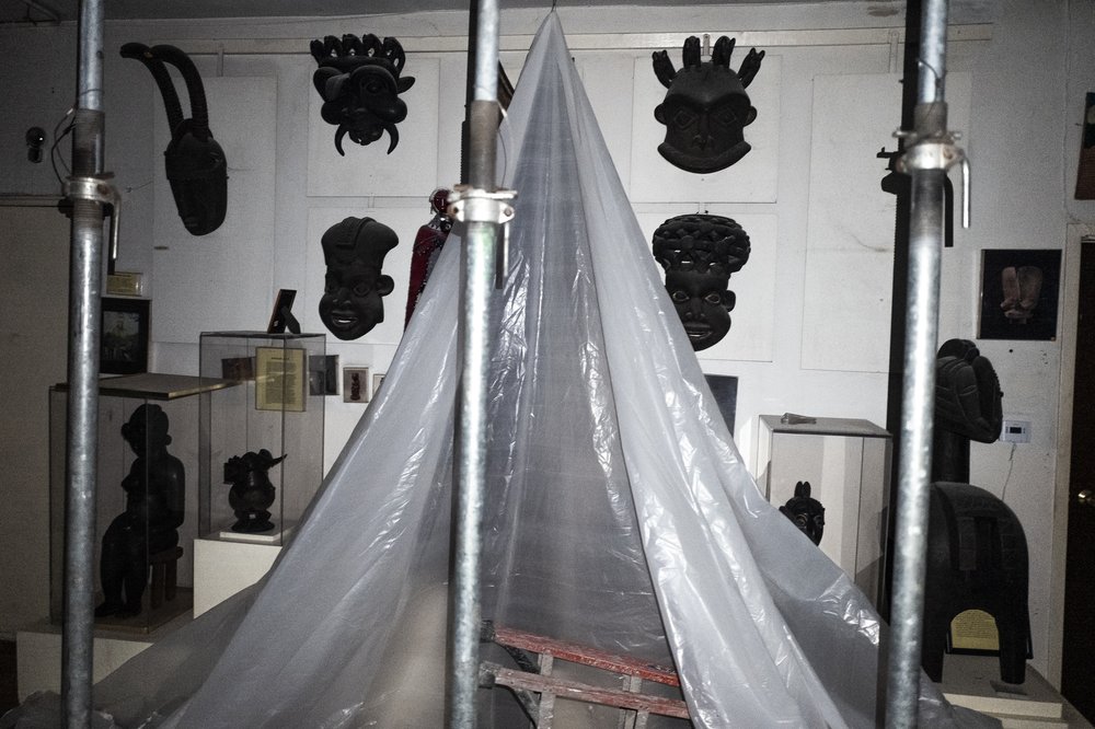 African masks hang on a wall draped in protective plastic.