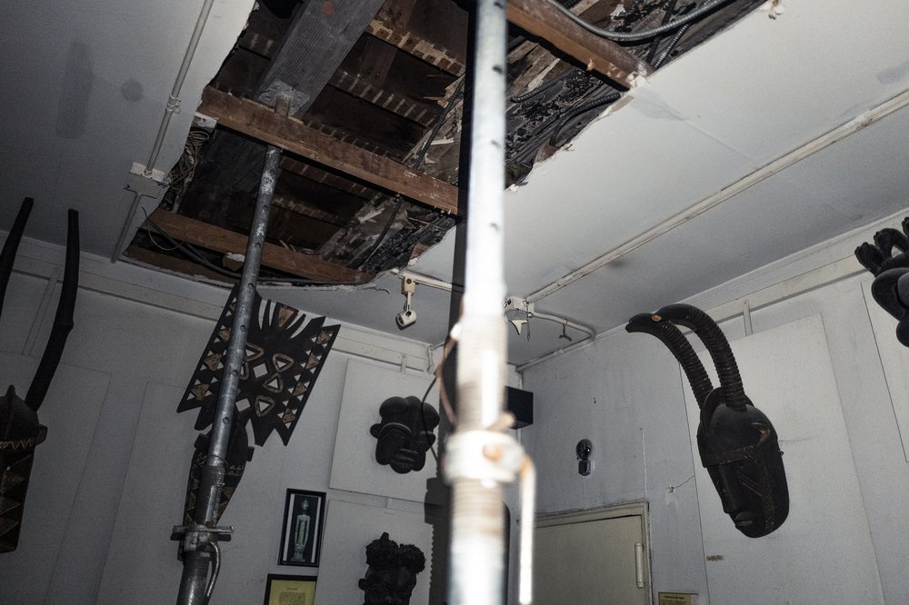 A removed ceiling above a wall of African art.