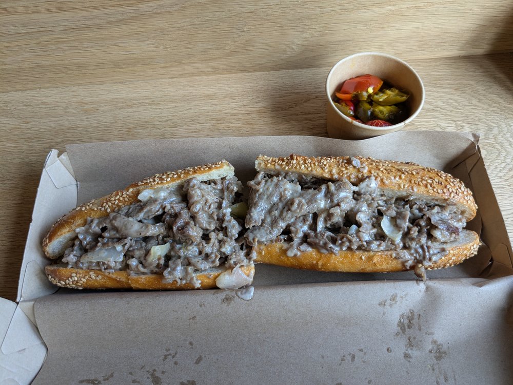 A sandwich in a box with sauce on the side.