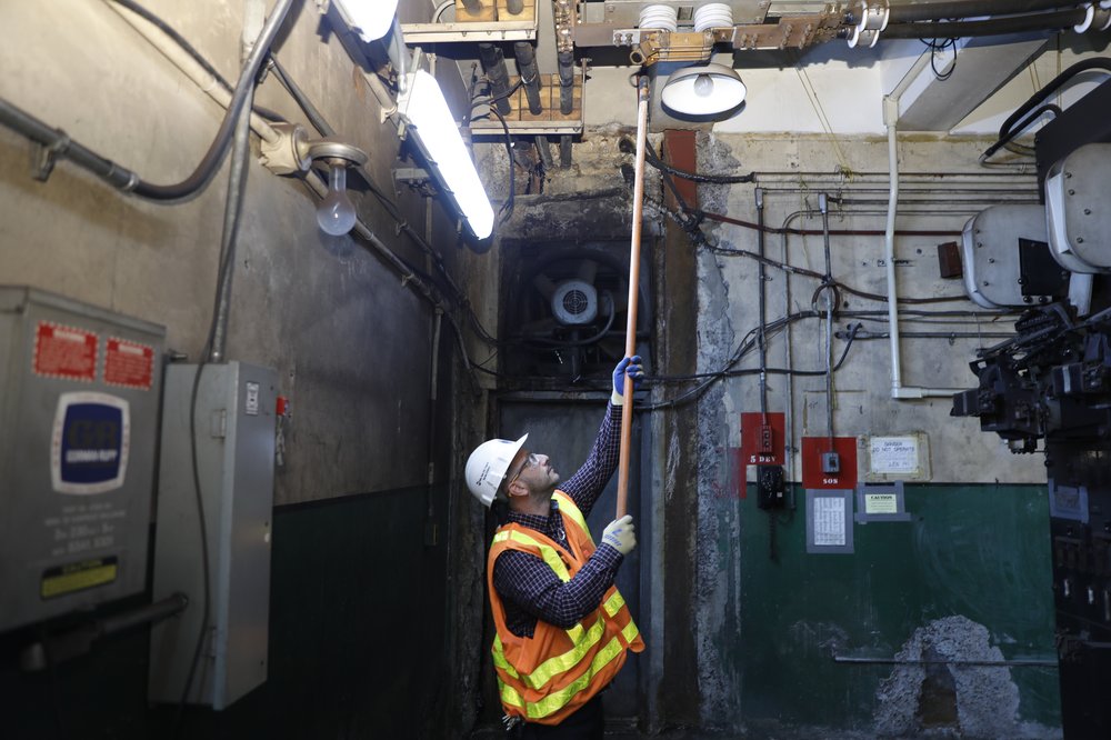 A man presses a button on a ceiling with a stick inside a dingy bunker.
