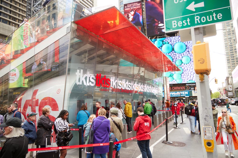 People standing in line at a glass booth with a red awning