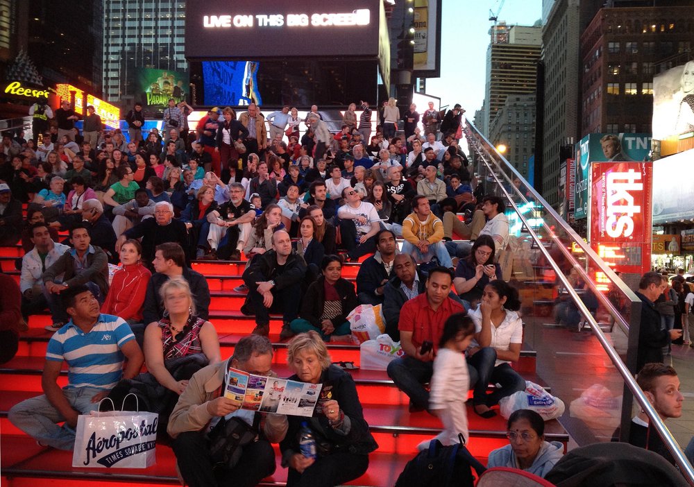 A crowd of people gathered on a bright red staircase on a city street