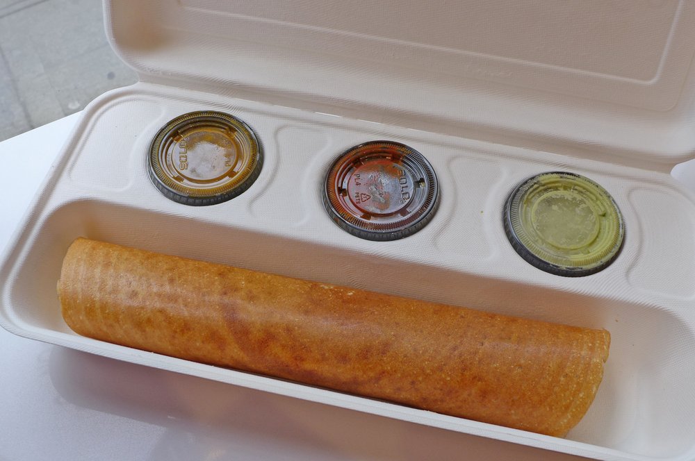 A dosa with three condiments on the side in a takeout container.