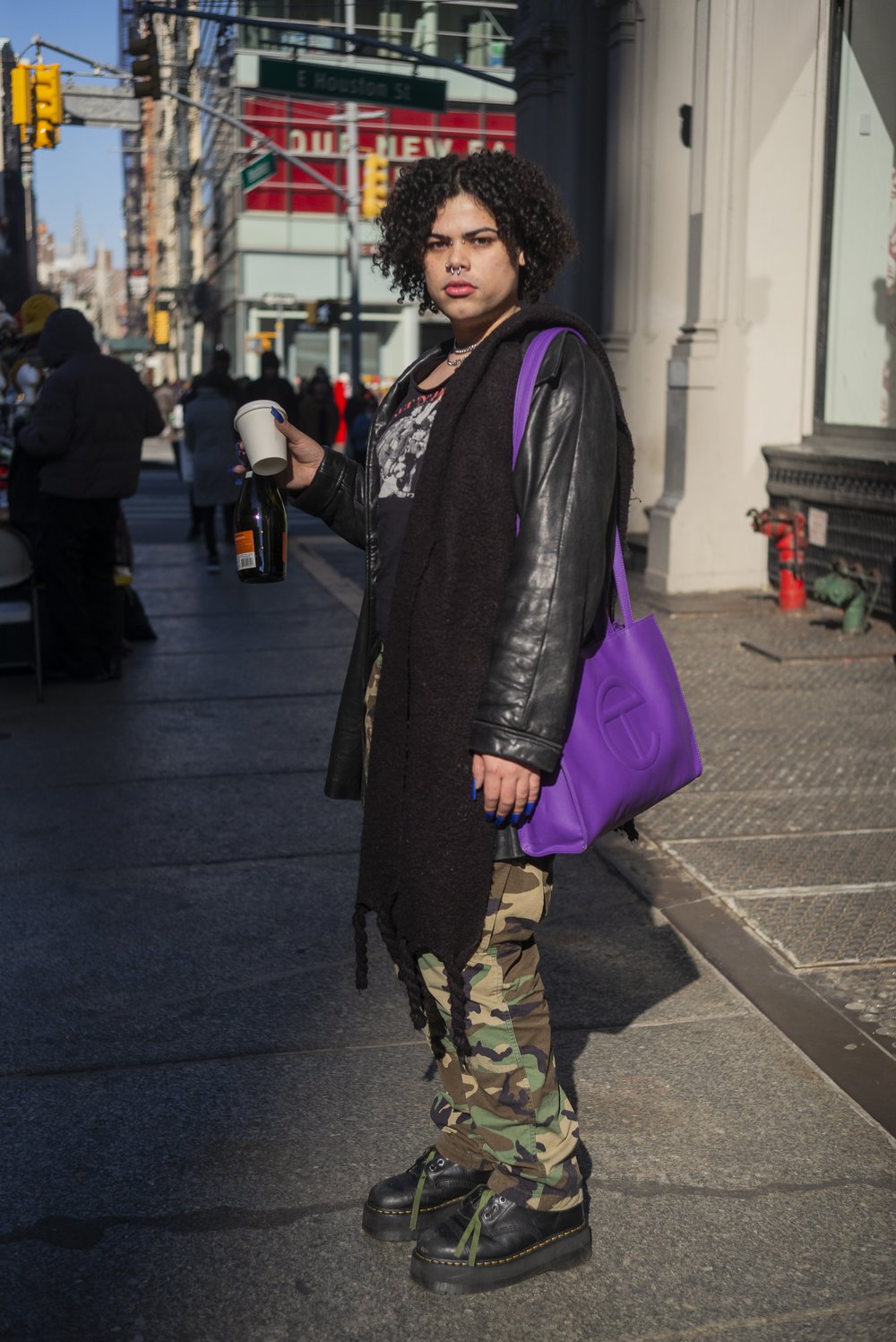 A women poses on a New York City sidewalk wearing a purple Telfar bag.