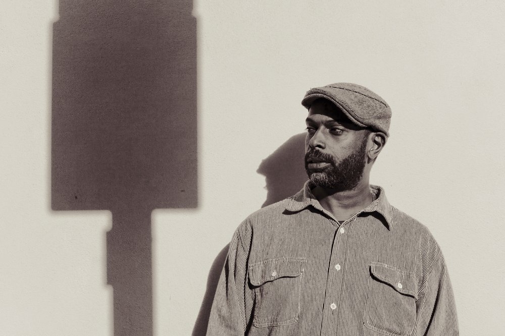 A man in a hat, standing next to the shadow of a loudspeaker