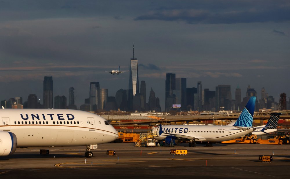A photo of United Airline flights on the tarmac at Newark Liberty International Airport during daylight in front of a dark and cloudy Manhattan skyline