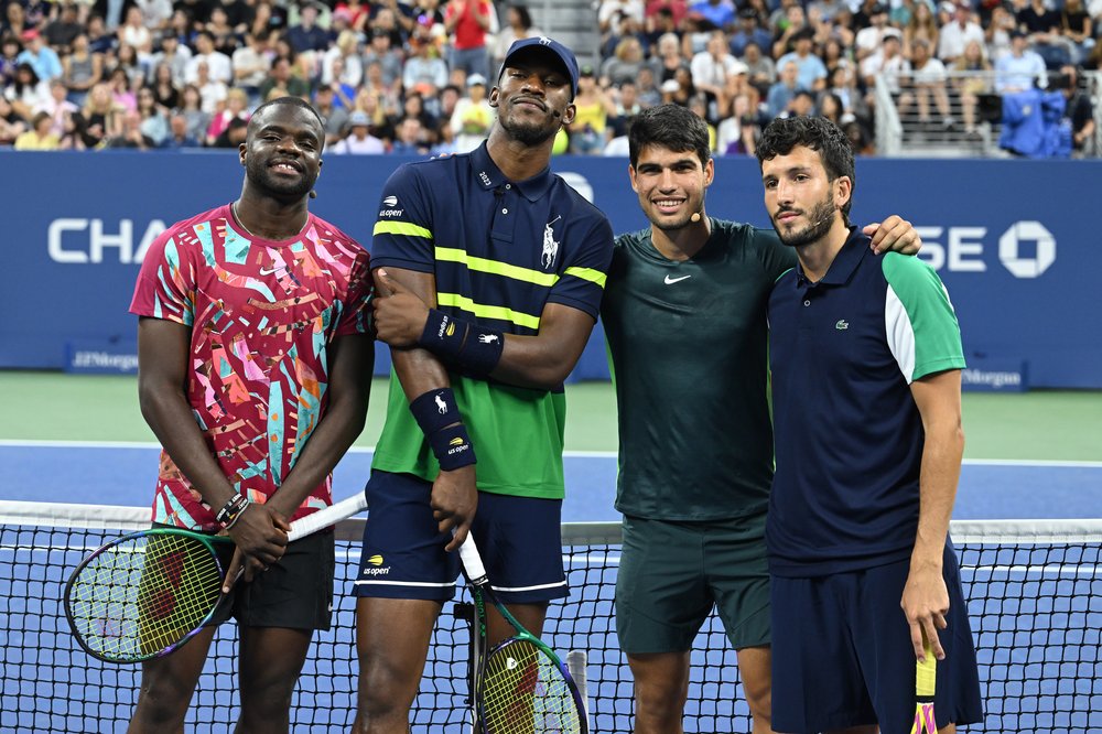 Four people pose for the camera by the net of a tennis court.