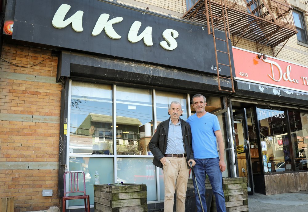 Two men stand in front of a storefront that says "Ukus."