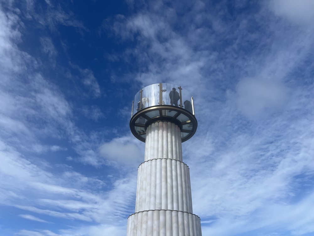 A column stands against a blue sky with people walking on.
