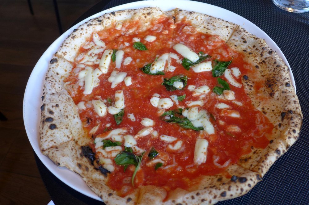 A thin crust pizza hanging off a plate.