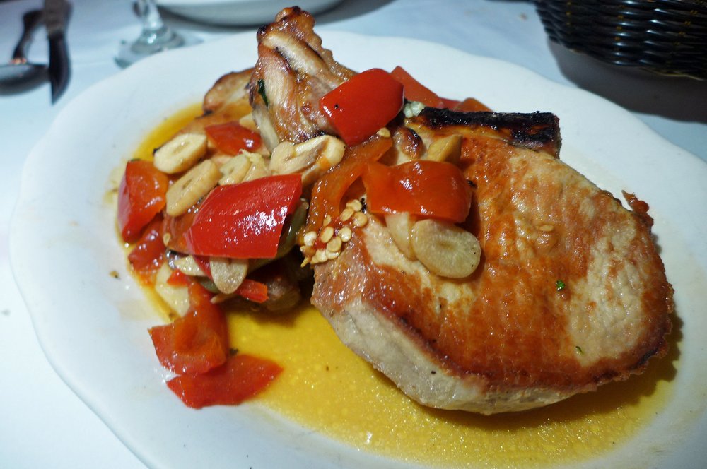 A large slice of a pork shop with peppers on top and served on a bed of sauce.