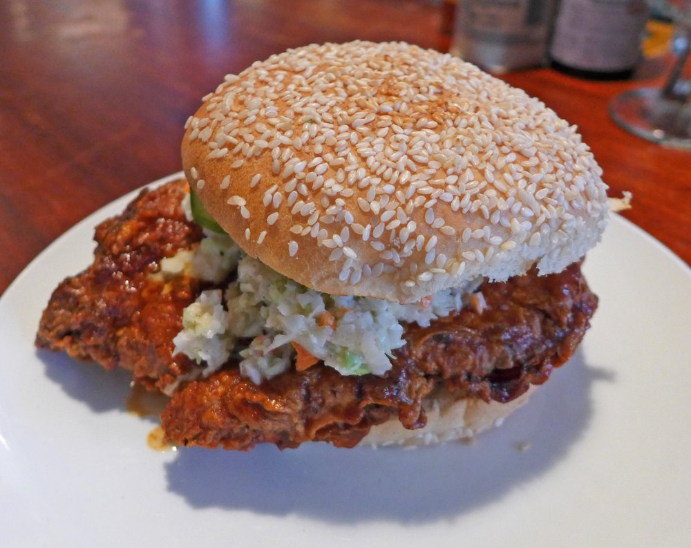 A fried chicken sandwich in a sesame-seed bun on a white plate.