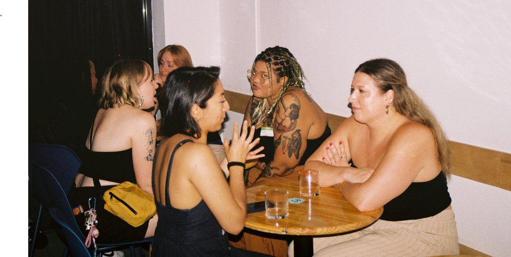 Women talk to each other at small tables in a bar.