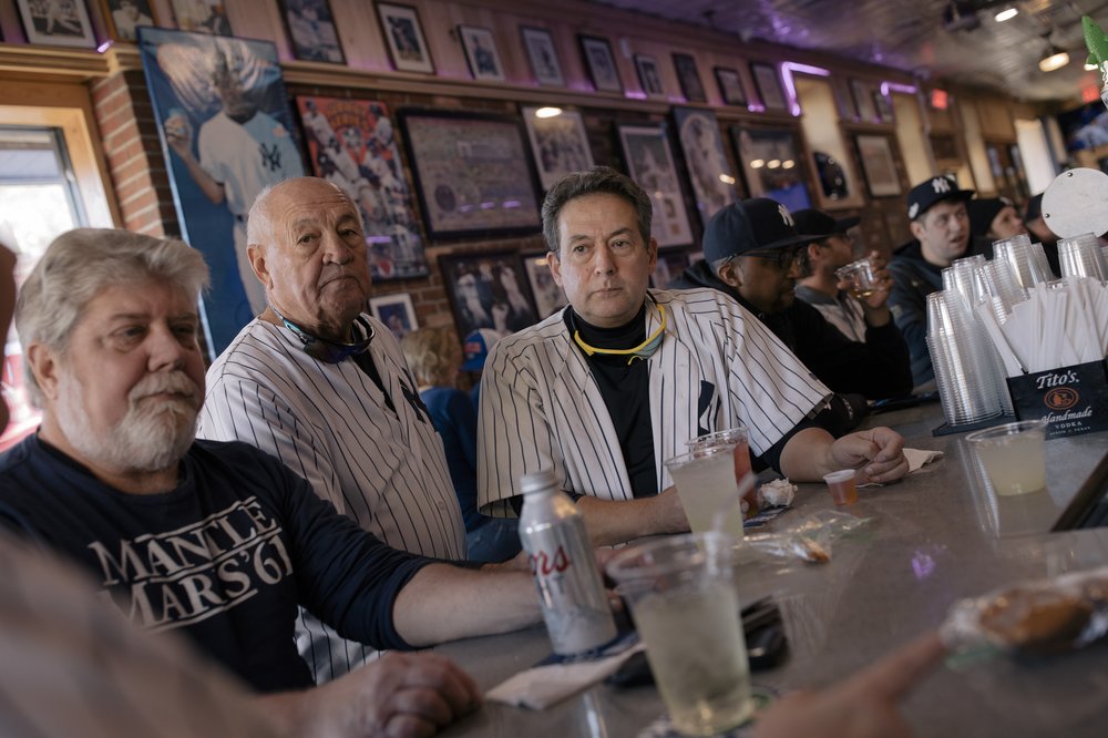 Don Bridges, center, listens on as Andra Gribulis, John Connor, left, Lou DiLullo, right, and members of the Yankee fan cohort go over possible lineup strategy and enjoy pregame drinks before the start of the Yankees playoff game against the Houston Astros in New York City, New York, U.S., on Saturday, October 22, 2022.