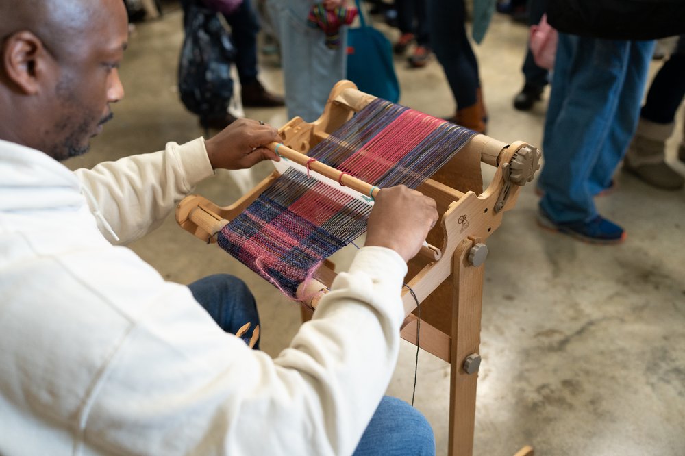 a man sits at a rigid heddle loom