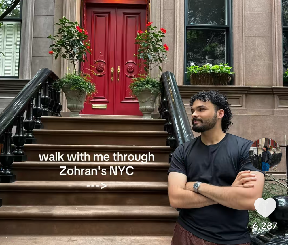 A man stands on the steps of a brownstone with a red door.