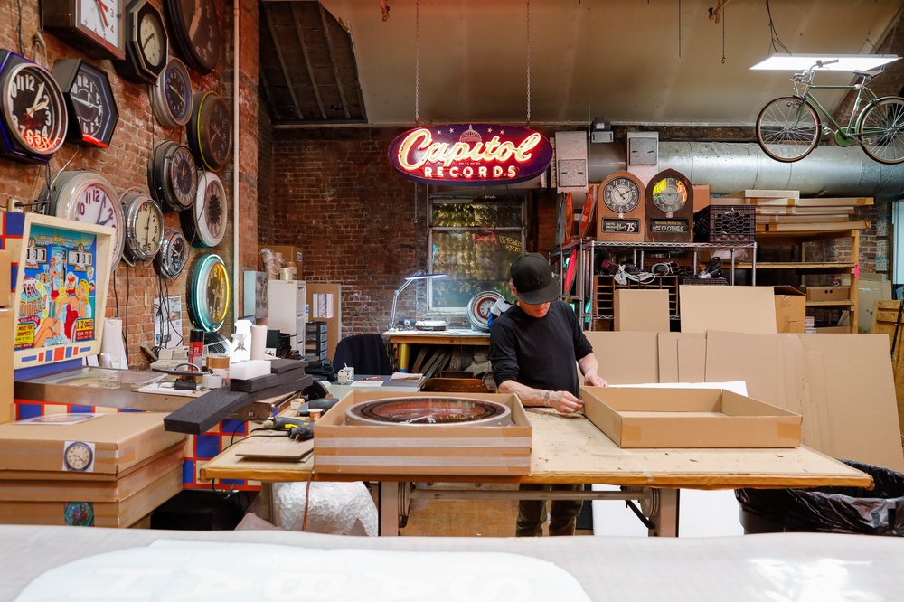 A man inside a store filled with vintage neon clocks.