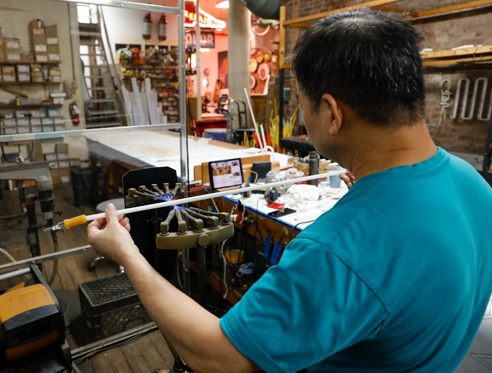 A man with a blue shirt looks at a thin neon tube.