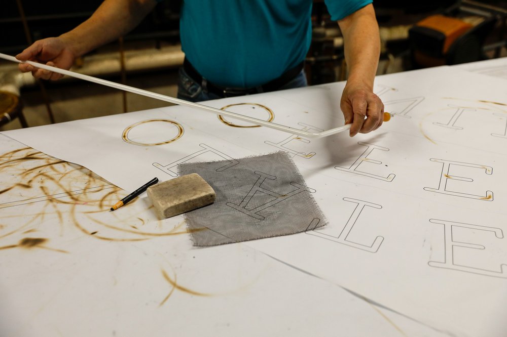 A man twists neon tubes over a work desk.