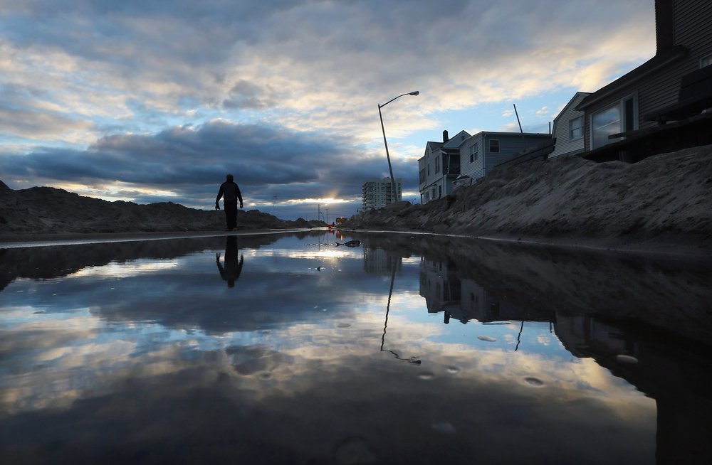 a59ffb3a1gettyimages-155404645-jpg.jpeg A man walks next to standing water and piles of sand swept onto a road from Superstorm Sandy at Rockaway Beach on November 3, 2012 in Queens. <br/>