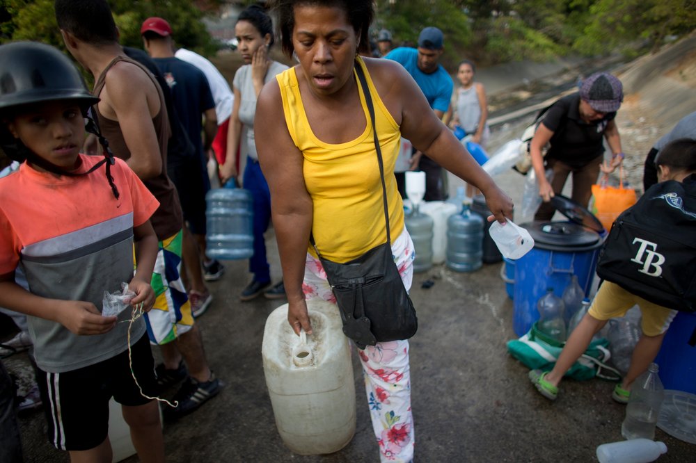 be146e2cb10150689i-jpg.jpeg A woman carries a container with water collected from an open pipe above the Guaire River, during rolling blackouts which affects the water pumps in people's homes, offices and stores, in Caracas, Venezuela. </br>(Ariana Cubillos/AP/Shutterstock)