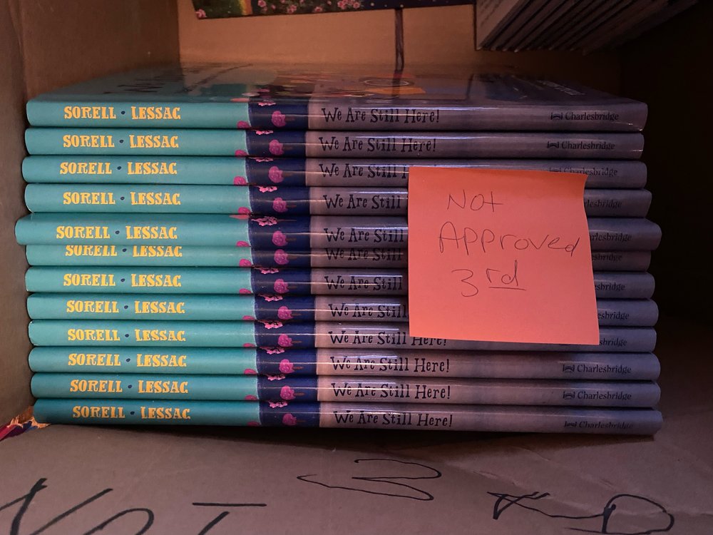 Copies of a book called "We Are Still Here!" in a box, along with a sticky note reading "Not approved 3rd."