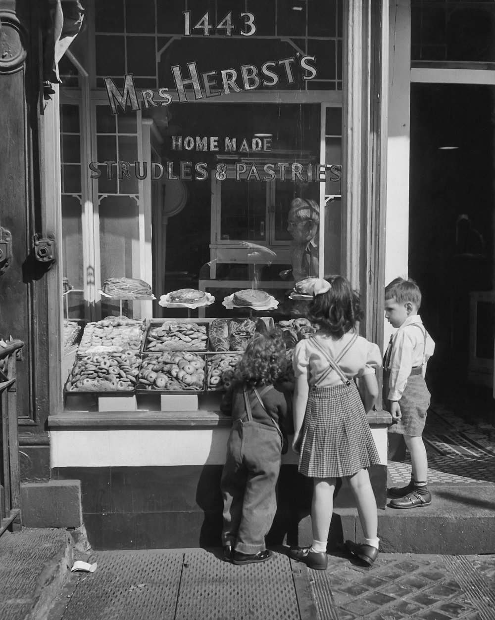 c08a6dec9.jpeg "Three children stand and look in the window of Mrs Herbst's bakery. 1960."