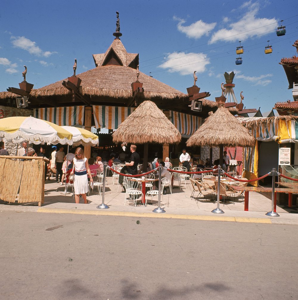 c8316beb7.jpeg "People relax and sit under grass umbrellas at an outdoor cafe at the World's Fair, Flushing Meadow, Queens. 1964."