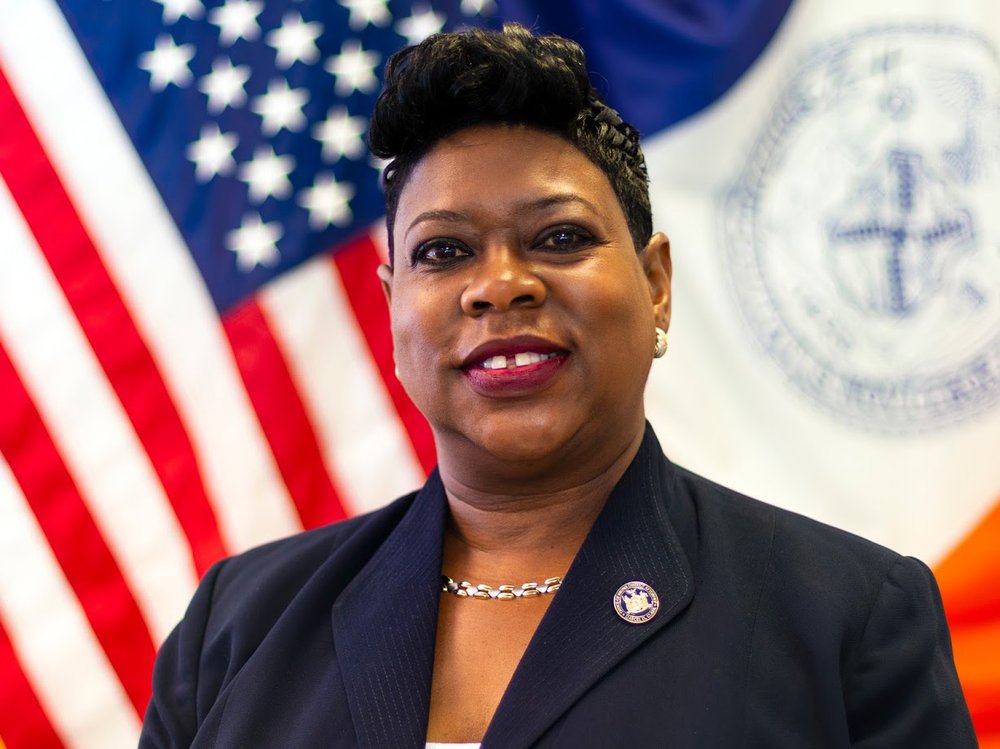 Photograph of Darcel Clark in front of the U.S. flag and NYC flag.