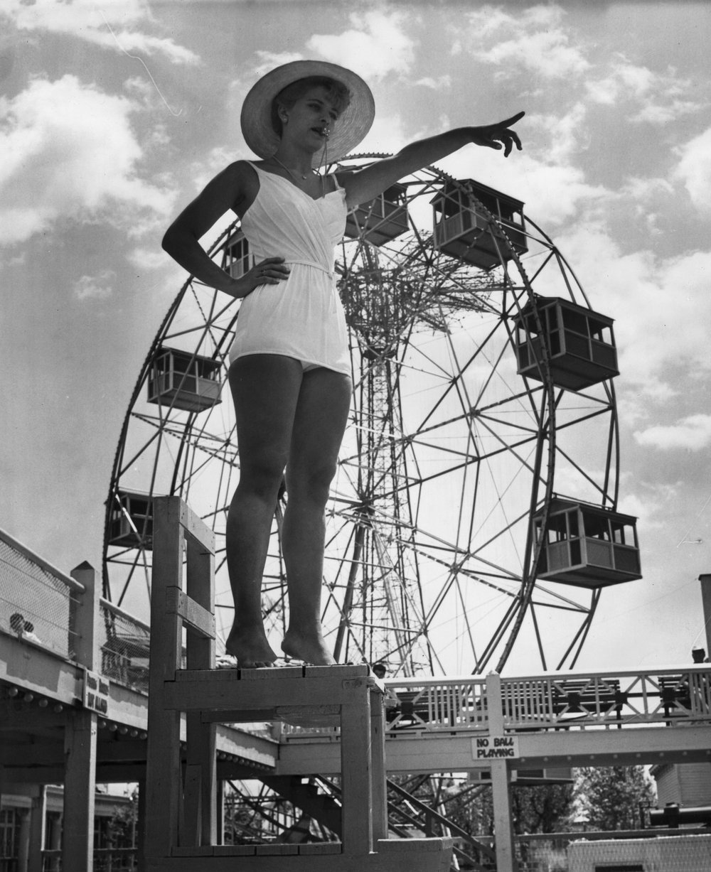 e78d62b12.jpeg "A lifeguard at Steeplechase park, Coney Island stands with a whistle between her lips as she points to a transgressor in the pool below. In the background is a fairground big-wheel. July 1961."