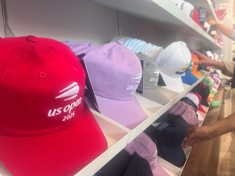 Red, lilac, gray and white hats with the U.S. Open logo are lined up on a shelf for sale.